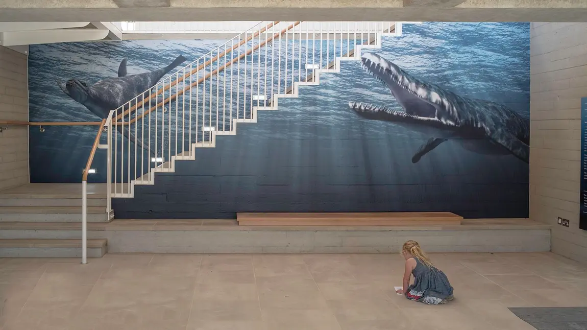 A little girl in front of the image of Jurassic marine life