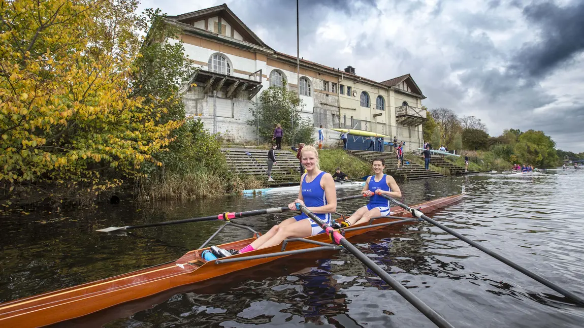 Polly Swann and Caitie Gorton-Phillips in a boat in front of the boathouse