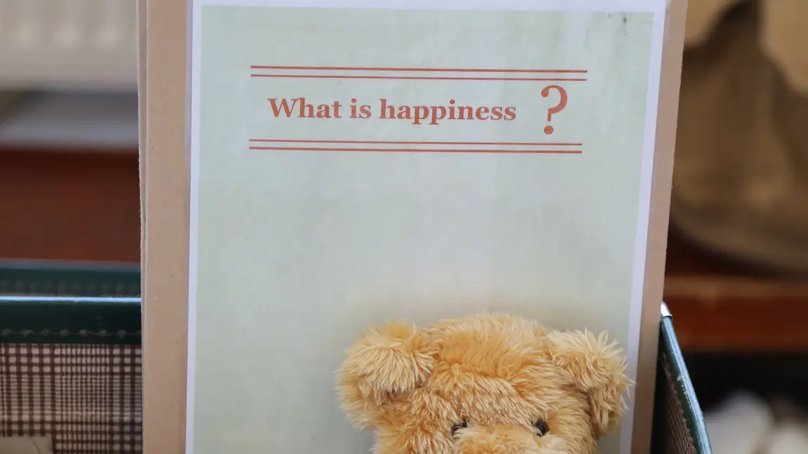 Teddy bear in front of page saying 'what is happiness?'