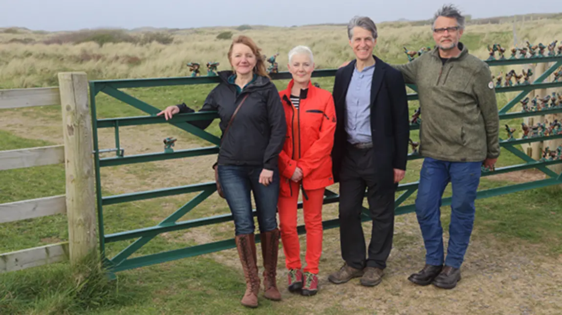 Four people stand in front of a fence