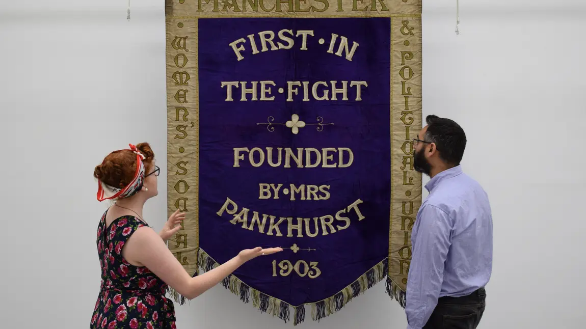 Celebrating the local voices of Women’s Suffrage Helen Antrobus & Adam Jaffer from the People's History Museum with the Manchester suffragette banner