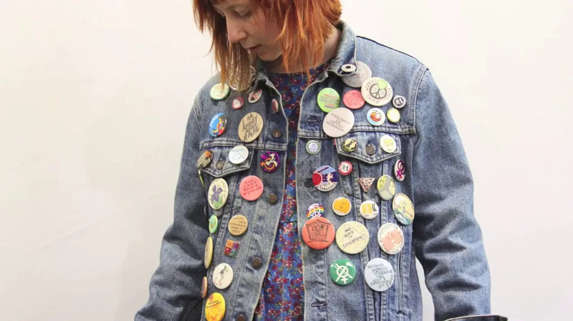 A young woman wearing a denim jacket covered in badges