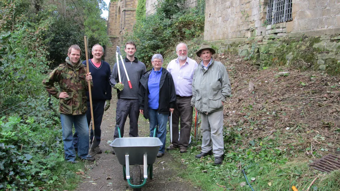 A group of volunteers with gardening tools stand by the cathedral walls
