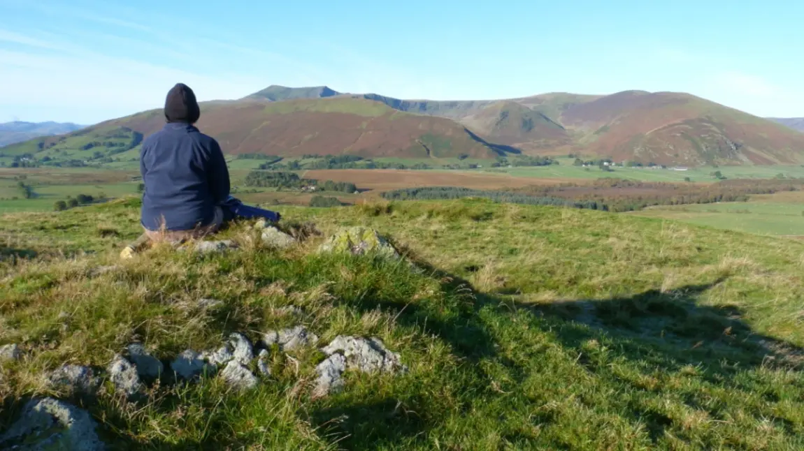 A person sitting on a rock looking towards a hill called Blencathra 