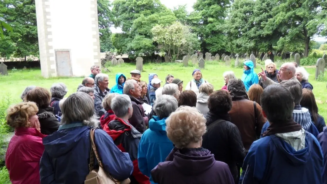 A group of people wearing outdoor clothes take part in a churchyard heritage walk at St Matthew's Churchyard