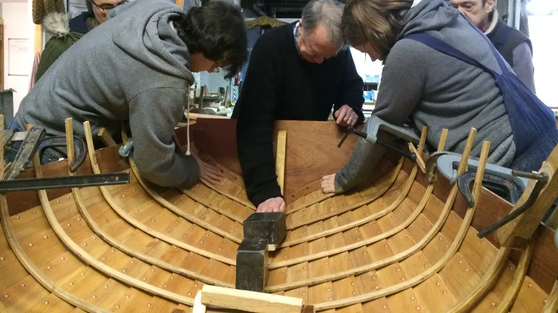 People working on the inner side of the hull of a wooden boat