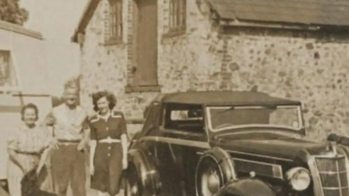 An old photograph showing a car and three people in front of a house