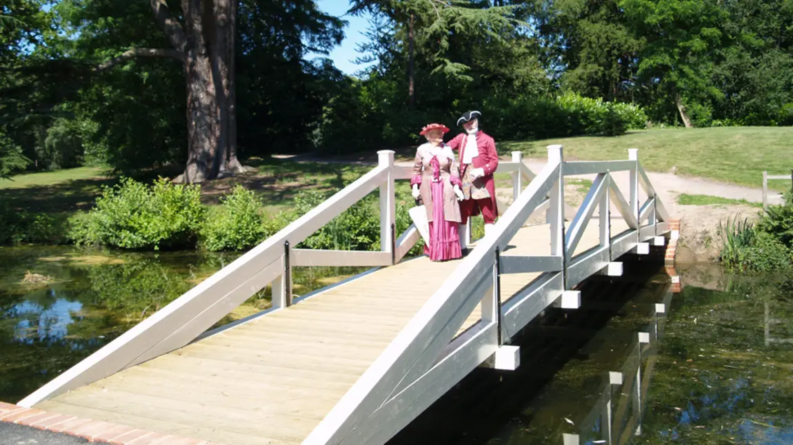 Two people in costume stand on a bridge in Painshill Park