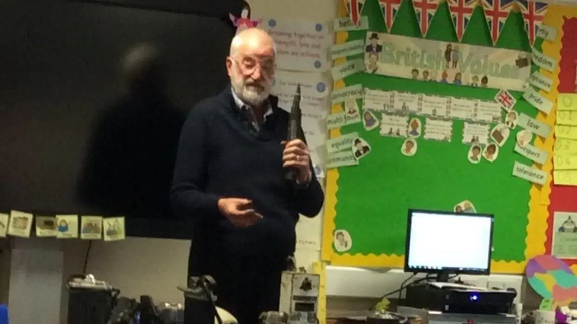 An older man with mining objects talking to a group of school children