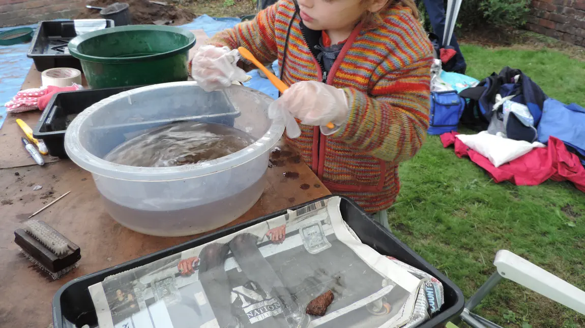 A child using a toothbrush to wash a sherd of pottery in a basin of water