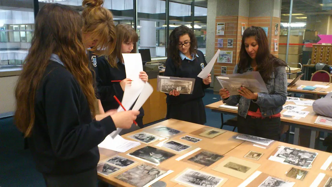 A group of young women standing around a table covered in old photographs