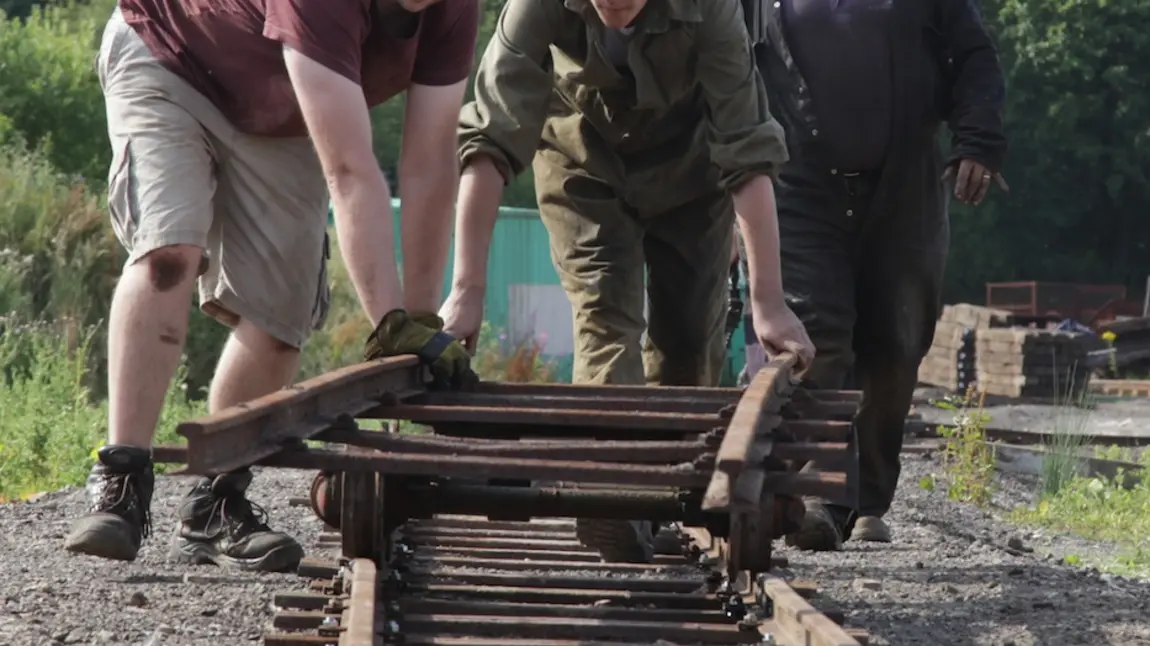 Two teenage trainees lay a new railway track by hand supervised by an older volunteer