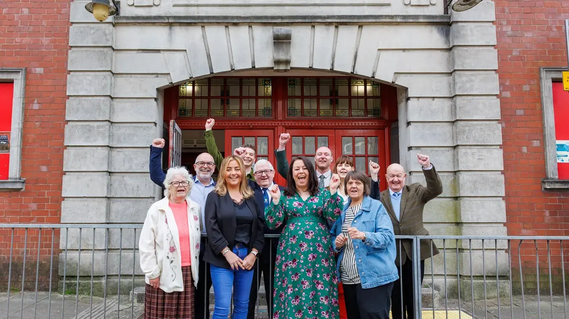 The Tylorstown community celebrate outside the Welfare Hall. A group of different ages from the Tylorstown community celebrate outside the Welfare Hall, smiling and raising their hands in the air.