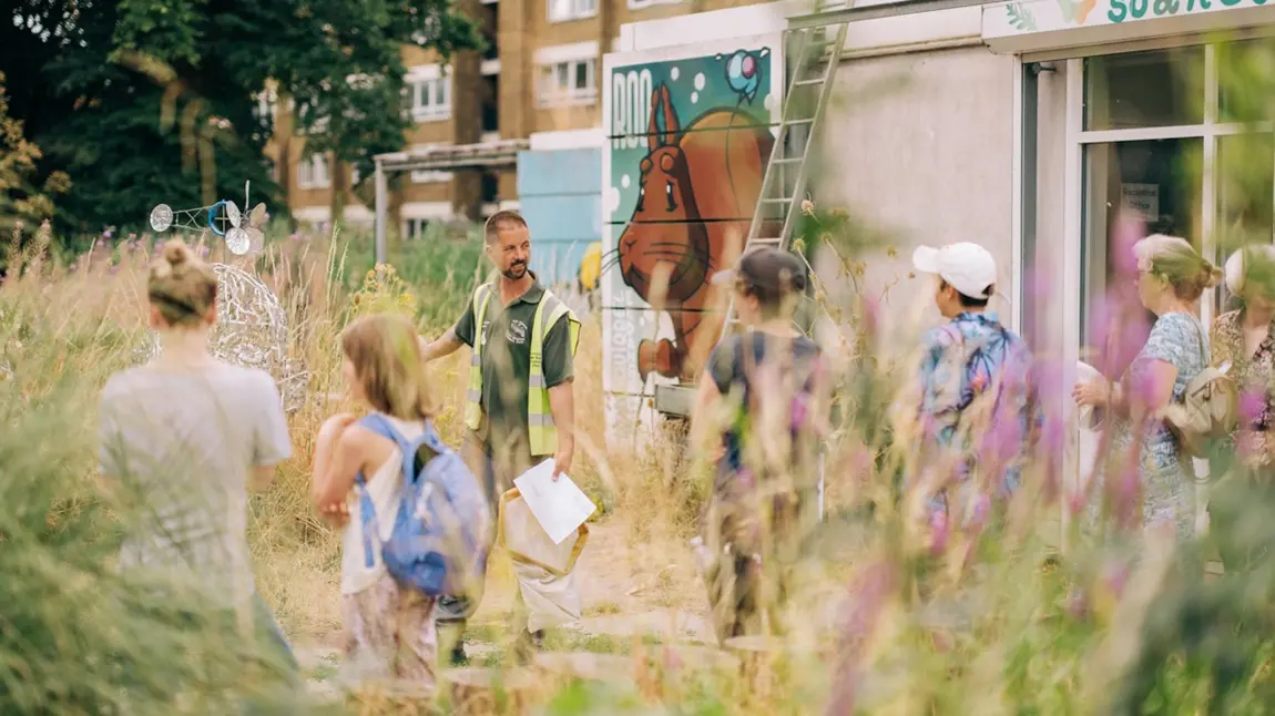 A guide wearing a high vis jacket shows a group of people around a lush meadow of long grass.
