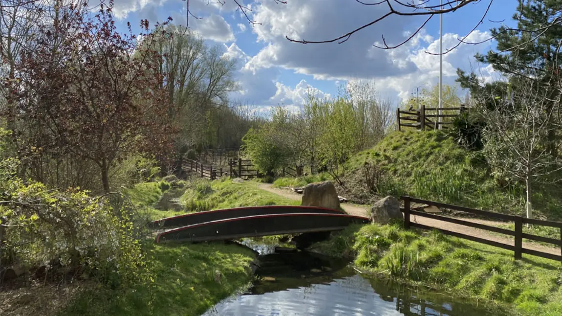 A pond with a bridge over it and footpath next to it on a sunny day