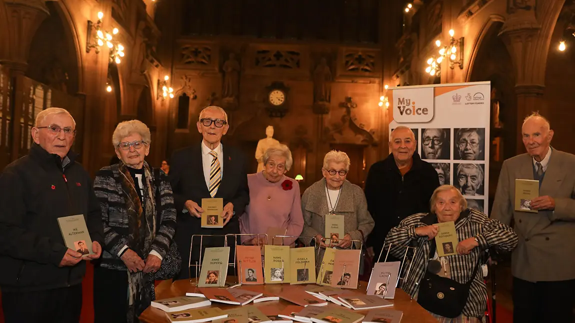 Holocaust survivors and refugees stand with their life story books in Sir John Rylands Library.