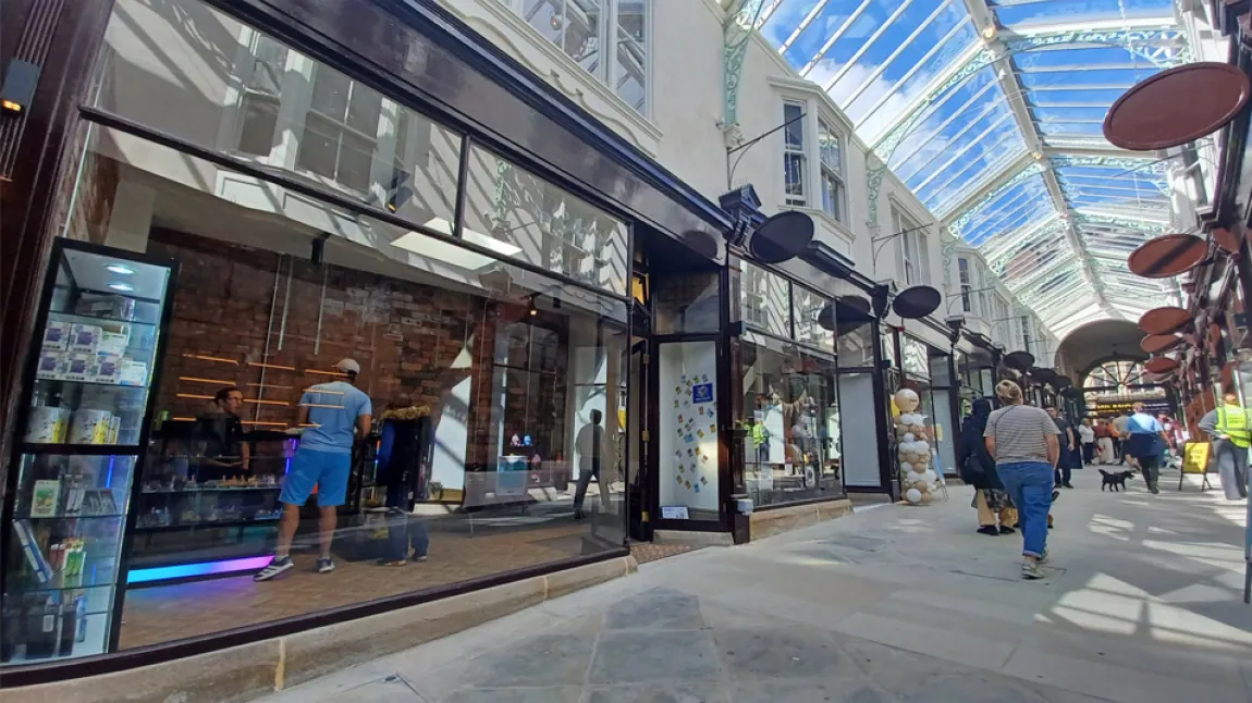 Inside Dewsbury Arcade, showing original timber shopfronts and a new glazed roof with shoppers walking down the central walkway