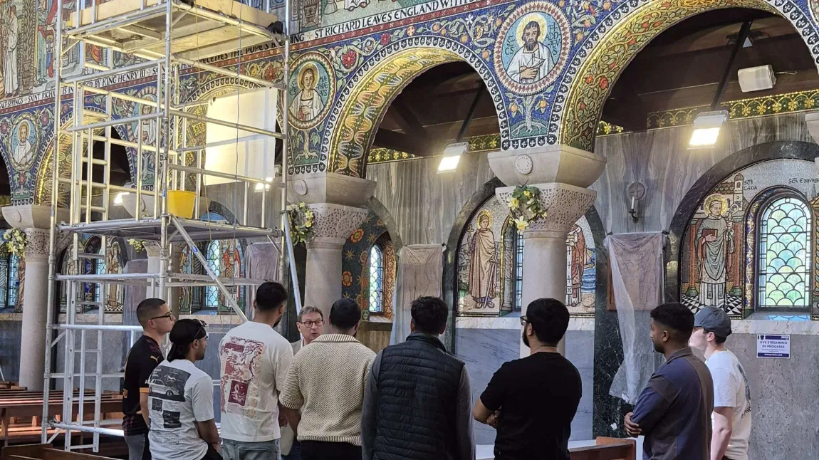 a group are given a tour of a church with mosaics under repair near a scaffolding tower
