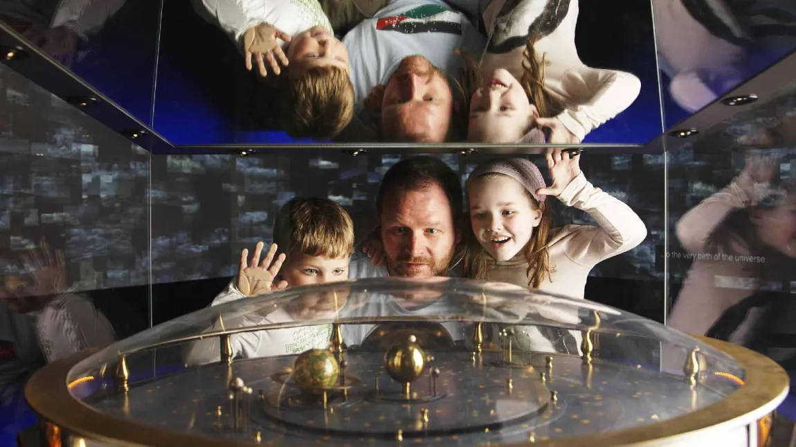 A man and two children look at a machine of an Earth spinning around the sun at the Royal Observatory Greenwich