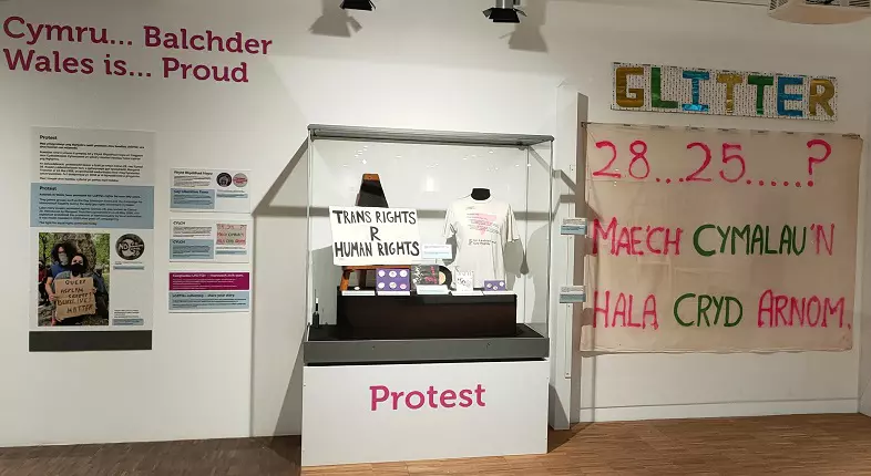 A museum space with various LGBTQ+ objects on display, such as protest banners, signs and photos