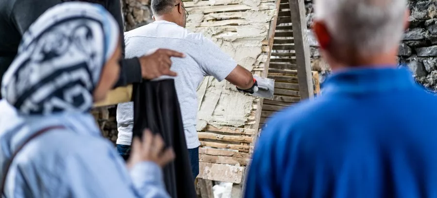 Two people watch on as a person applies plaster to a wooden structure at Calverley Old Hall