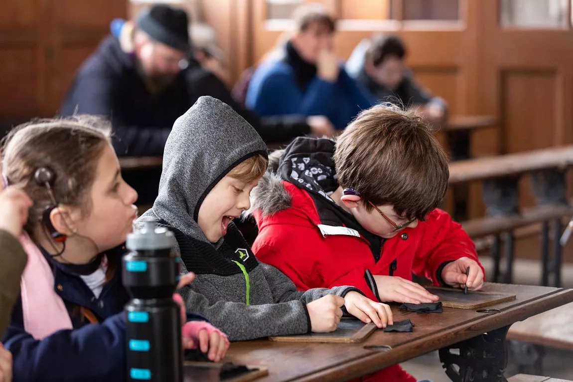 Children sitting at an old school desk and drawing on small black boards