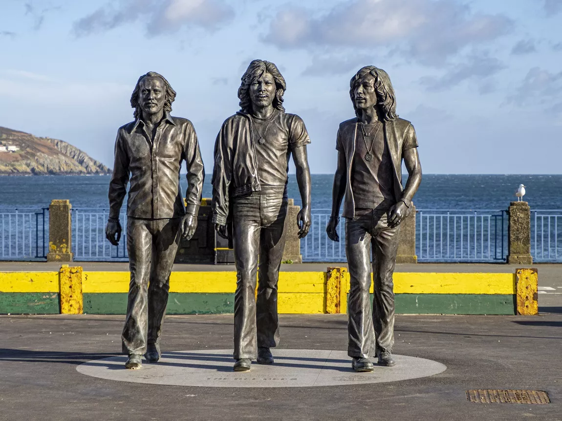 Three bronze statues of the Bee Gees, standing on the sea front in 1970s clothing 