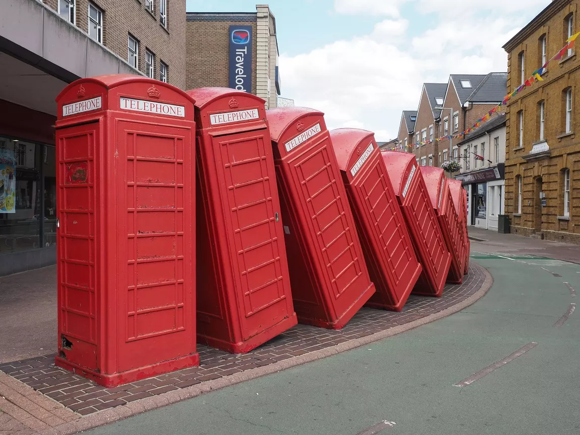 Traditional red telephone boxes positioned leaning to the side and falling like dominos