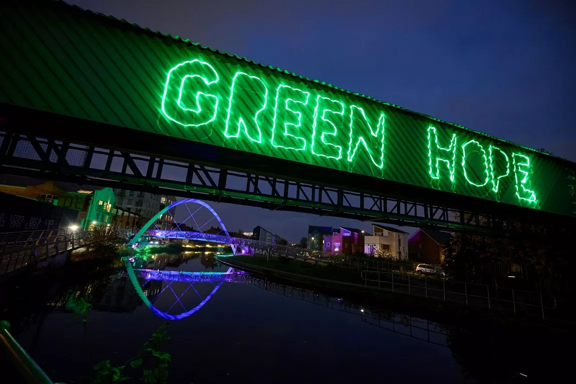 Coventry canal at night, with colourful lights illuminating the bridges. One sign reads 'Green Hope'.