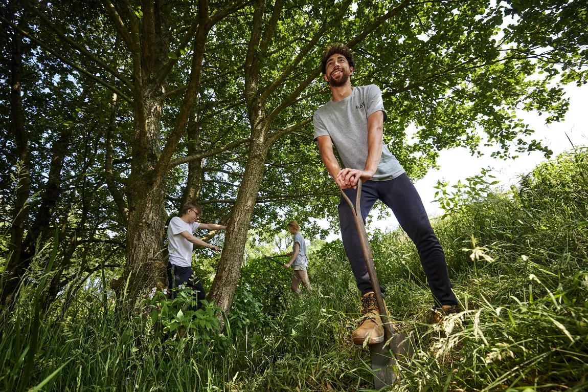 Young people working in nature, digging, sawing and trimming 