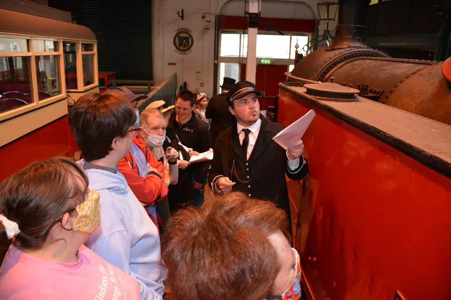 People listening to a tour guide as they point at an old train