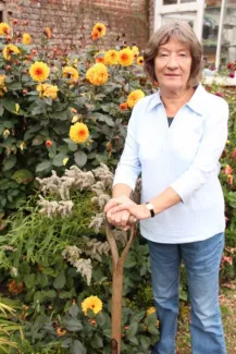 Woman standing with spade next to bright orange and yellow flowers