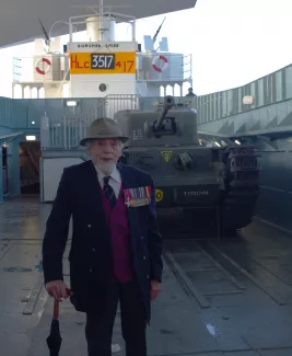 Elderly man with medals standing inside landing craft in front of tank